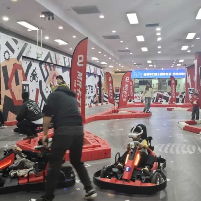 Racing go-karts indoor track with children and adults, vibrant entertainment at the MR Kart amusement center, dynamic play area with red accents, indoor go-kart racing facility at lekevrexport.com.