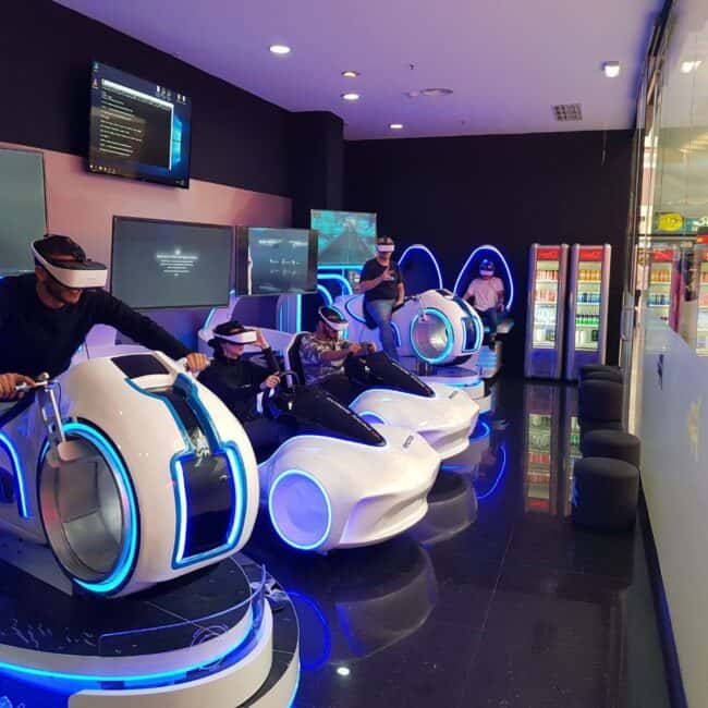 Futuristic virtual reality arcade with people wearing VR headsets and riding immersive motorcycle simulation games in a neon-lit gaming center.