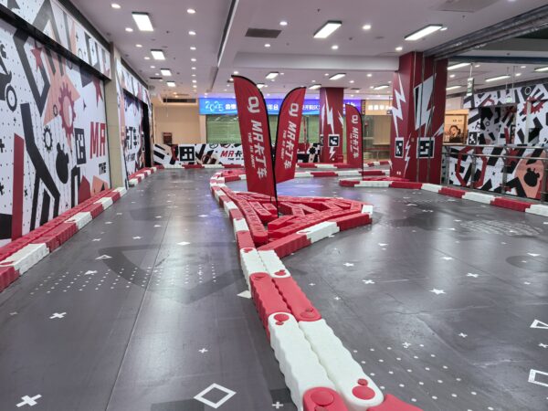 MR GO KART Indoor Racing Track Indoor go-kart racing track with vibrant red and white barriers, featuring sharp turns and dynamic design elements for an exciting racing experience.