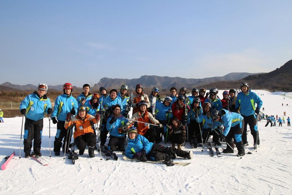 Contact 1 Group of skiers and snowboarders on a snowy mountain with clear blue sky and mountain range in the background, enjoying a winter sports day.